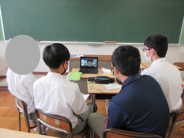 4人の生徒たちがラップトップPCを囲んで、オンライン会議に参加している様子