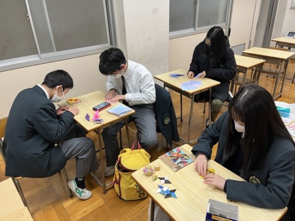 4人の生徒たちが4つの机に分かれてそれぞれ折り紙を作ったりイラストを描いたりしている様子