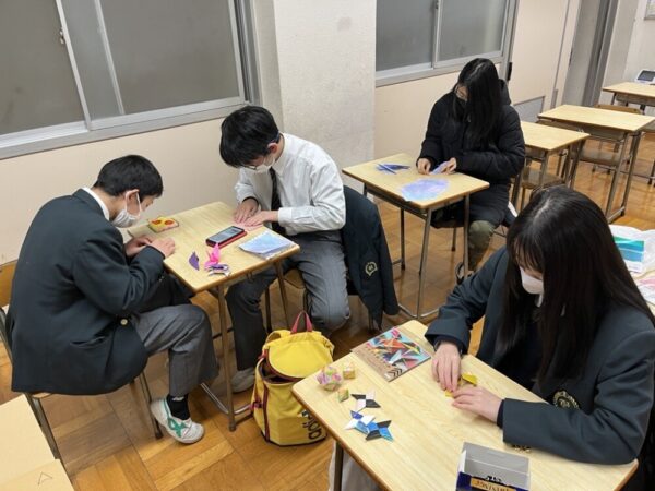 4人の生徒たちが4つの机に分かれてそれぞれ折り紙を作ったりイラストを描いたりしている様子